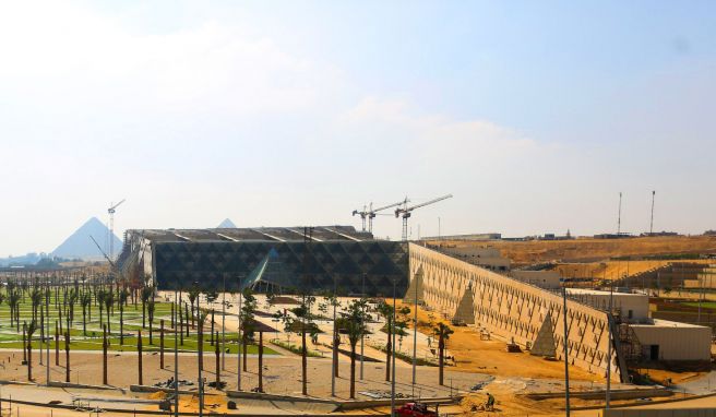 Das Große Ägyptische Museum wird ein kolossales Bauwerk. Hinter ihm sieht man die Pyramiden von Giseh auf einem Plateau. 
